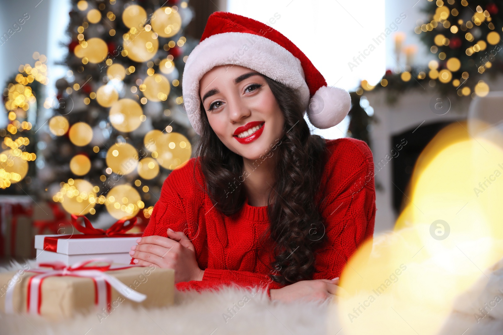 Photo of Beautiful woman wearing Santa hat with Christmas gifts on floor at home