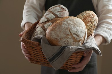 Photo of Man holding wicker basket with different types of bread on brown background, closeup