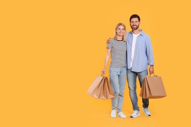 Photo of Family shopping. Happy couple with paper bags on orange background. Space for text