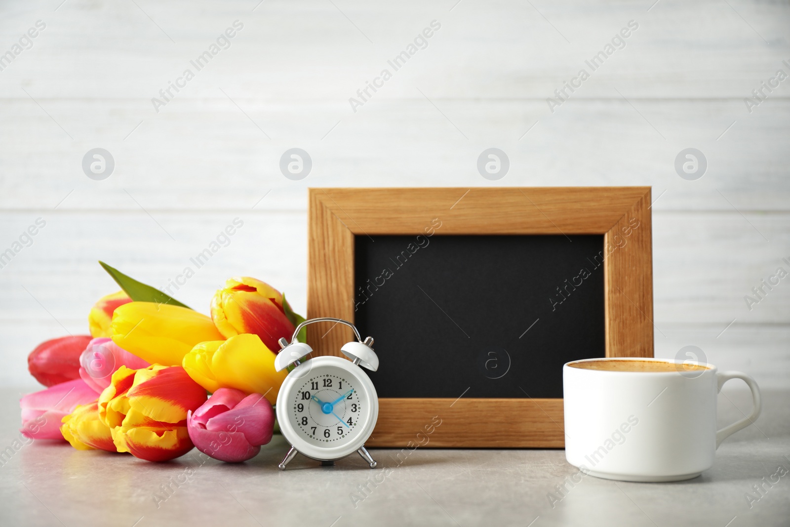 Photo of Chalkboard with morning wish, delicious coffee, tulips and alarm clock on light grey table