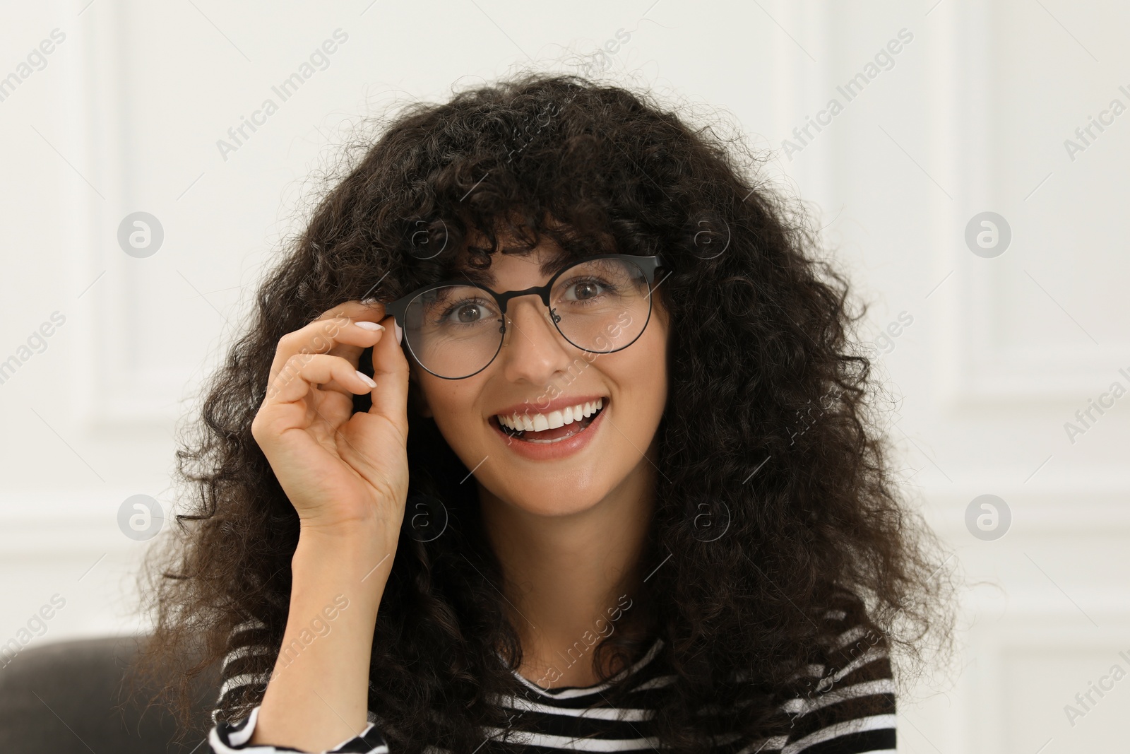 Photo of Portrait of beautiful woman with curly hair sitting on armchair indoors. Attractive lady smiling and looking at camera