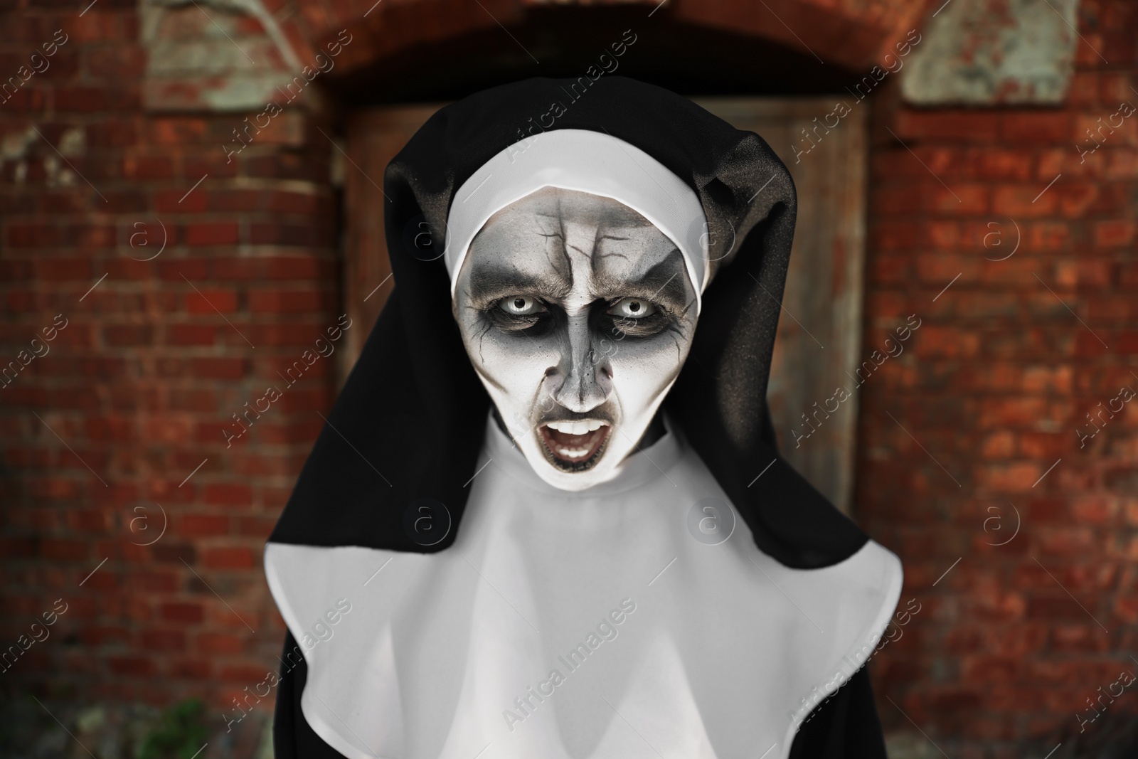 Photo of Portrait of scary devilish nun near red brick wall. Halloween party look