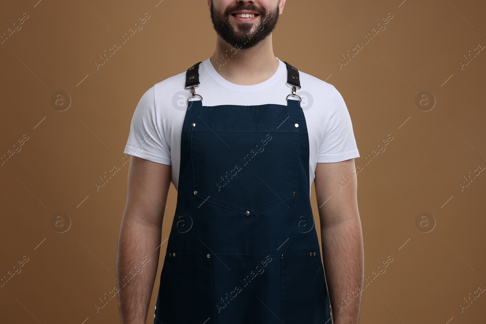 Photo of Smiling man in kitchen apron on brown background, closeup. Mockup for design