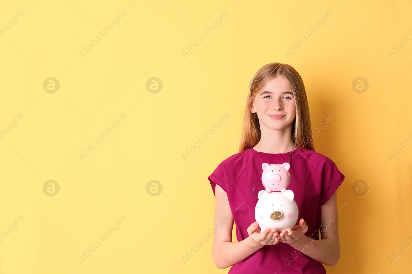 Photo of Teen girl with piggy banks on color background. Space for text