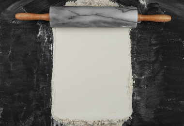 Flour and rolling pin on black table, top view. Space for text