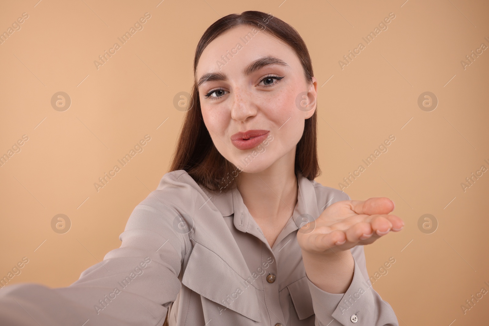 Photo of Beautiful woman taking selfie and blowing kiss on beige background