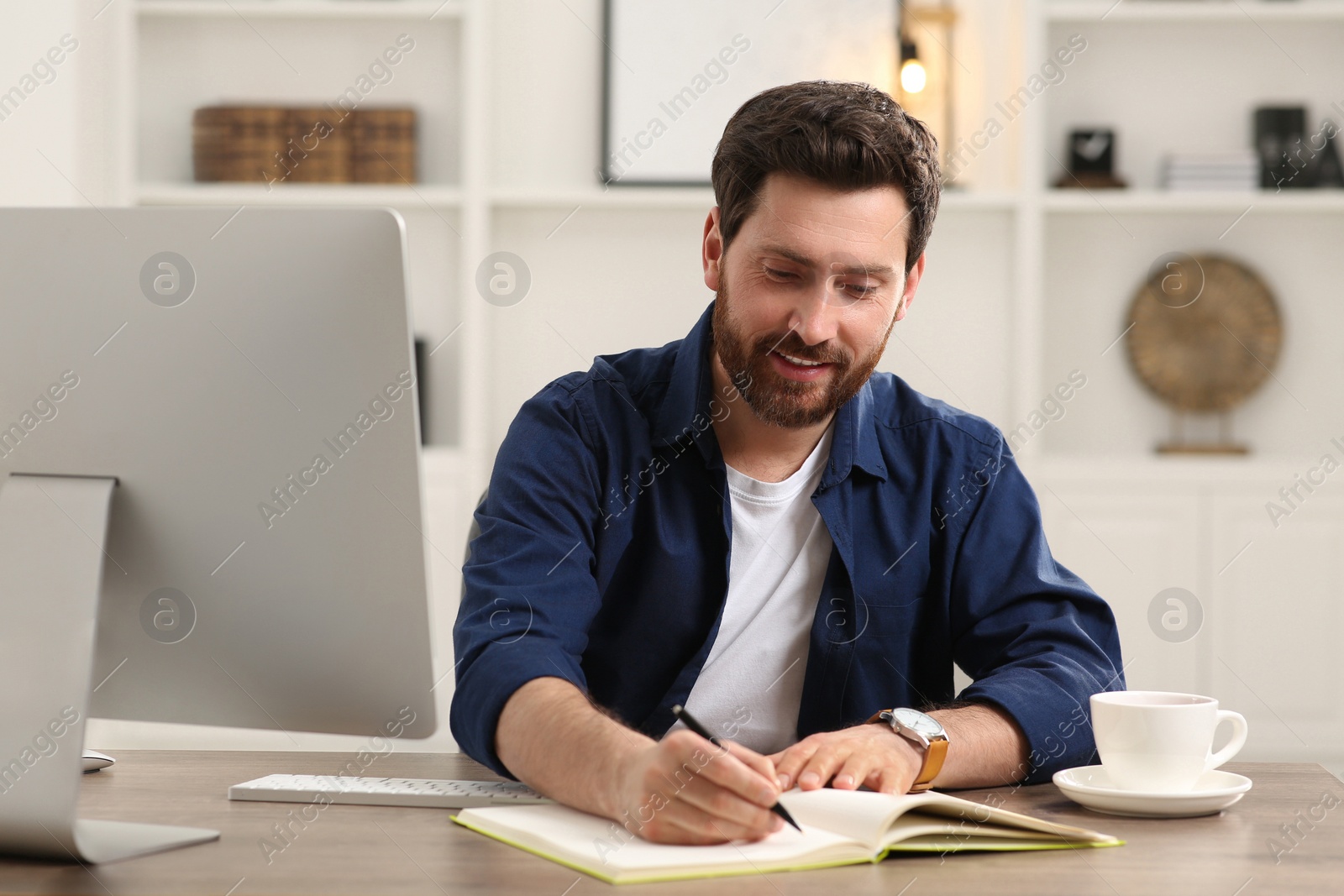 Photo of Home workplace. Happy man taking notes at wooden desk in room