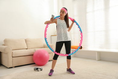 Photo of Lazy young woman with hula hoop and smartphone at home