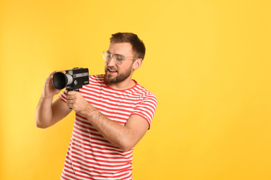 Young man with vintage video camera on yellow background, space for text