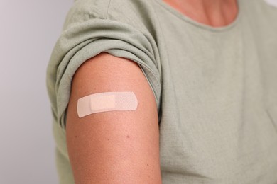 Photo of Woman with adhesive bandage on her arm after vaccination against light grey background, closeup