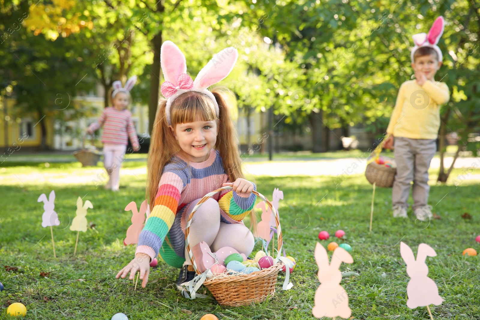 Photo of Cute little children hunting eggs in park. Easter tradition