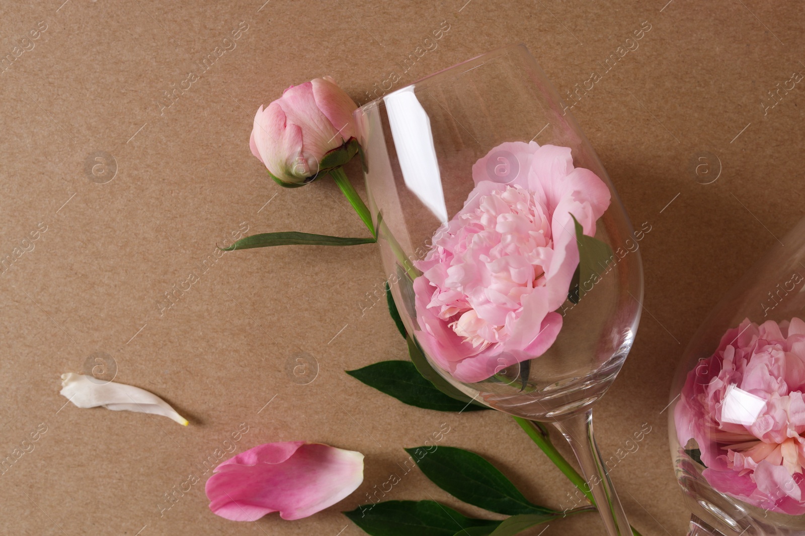 Photo of Wineglasses and beautiful pink peonies on brown background, flat lay
