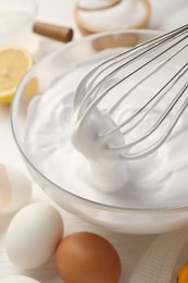 Photo of Bowl with whipped cream, whisk and ingredients on white wooden table, closeup