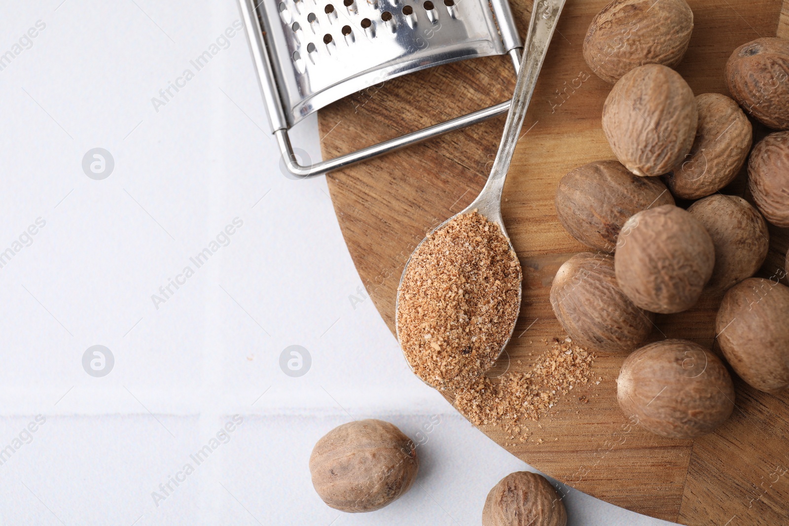 Photo of Spoon with grated nutmeg, seeds and grater on white table, flat lay. Space for text