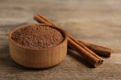 Photo of Aromatic cinnamon powder in bowl near sticks on wooden table, closeup