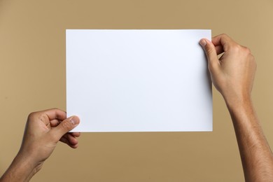Photo of Man holding sheet of paper on beige background, closeup. Mockup for design