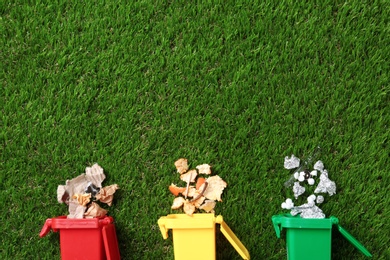 Photo of Trash bins and different garbage on green grass, top view with space for text. Waste recycling concept