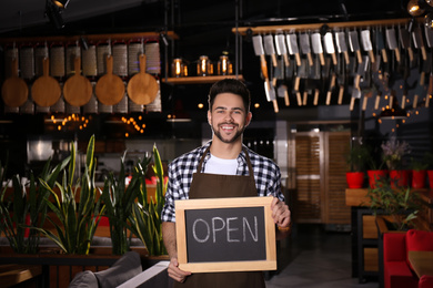 Young business owner holding sign OPEN in his cafe