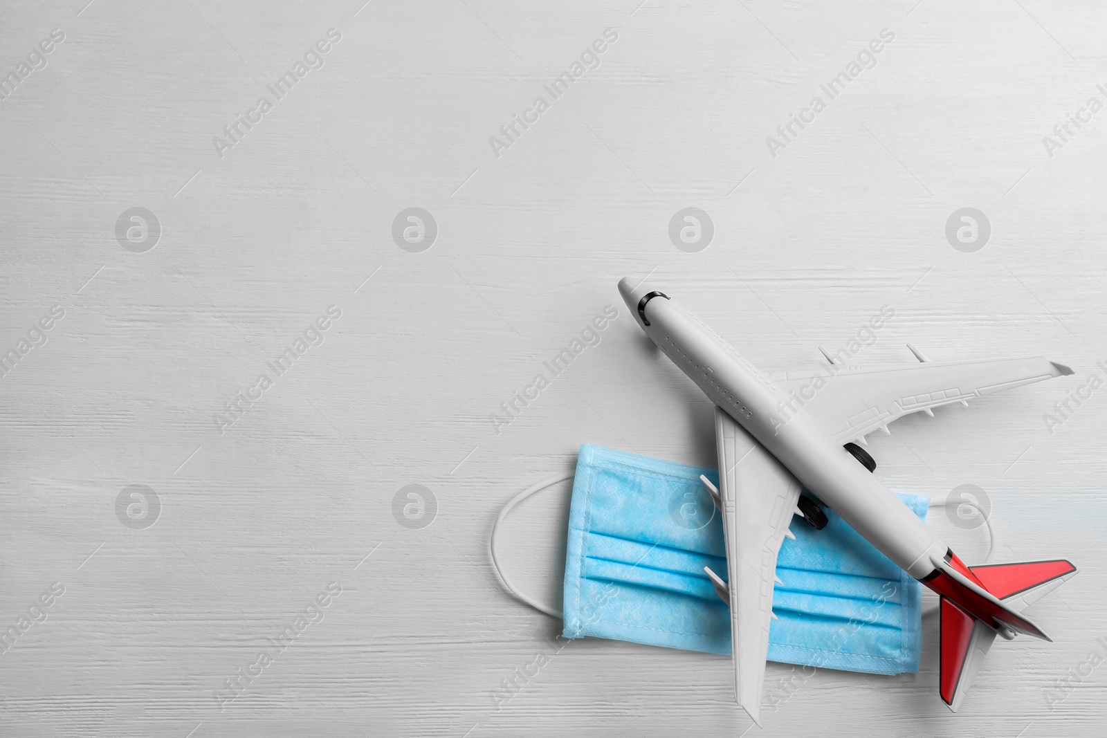 Photo of Toy airplane and medical mask on white wooden background, flat lay with space for text. Travelling during coronavirus pandemic