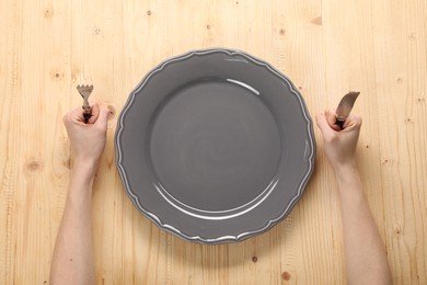 Photo of Woman with fork, knife and empty plate at wooden table, top view