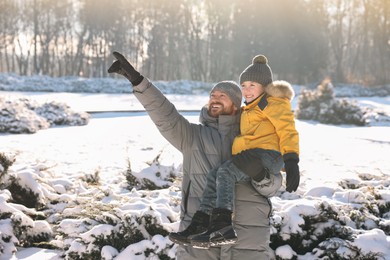Photo of Happy father pointing at something to his son in sunny snowy park