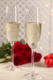 Beautiful engagement ring with gemstone in glass of sparkling wine and roses on white wooden table