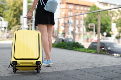 Young woman with yellow carry on suitcase outdoors