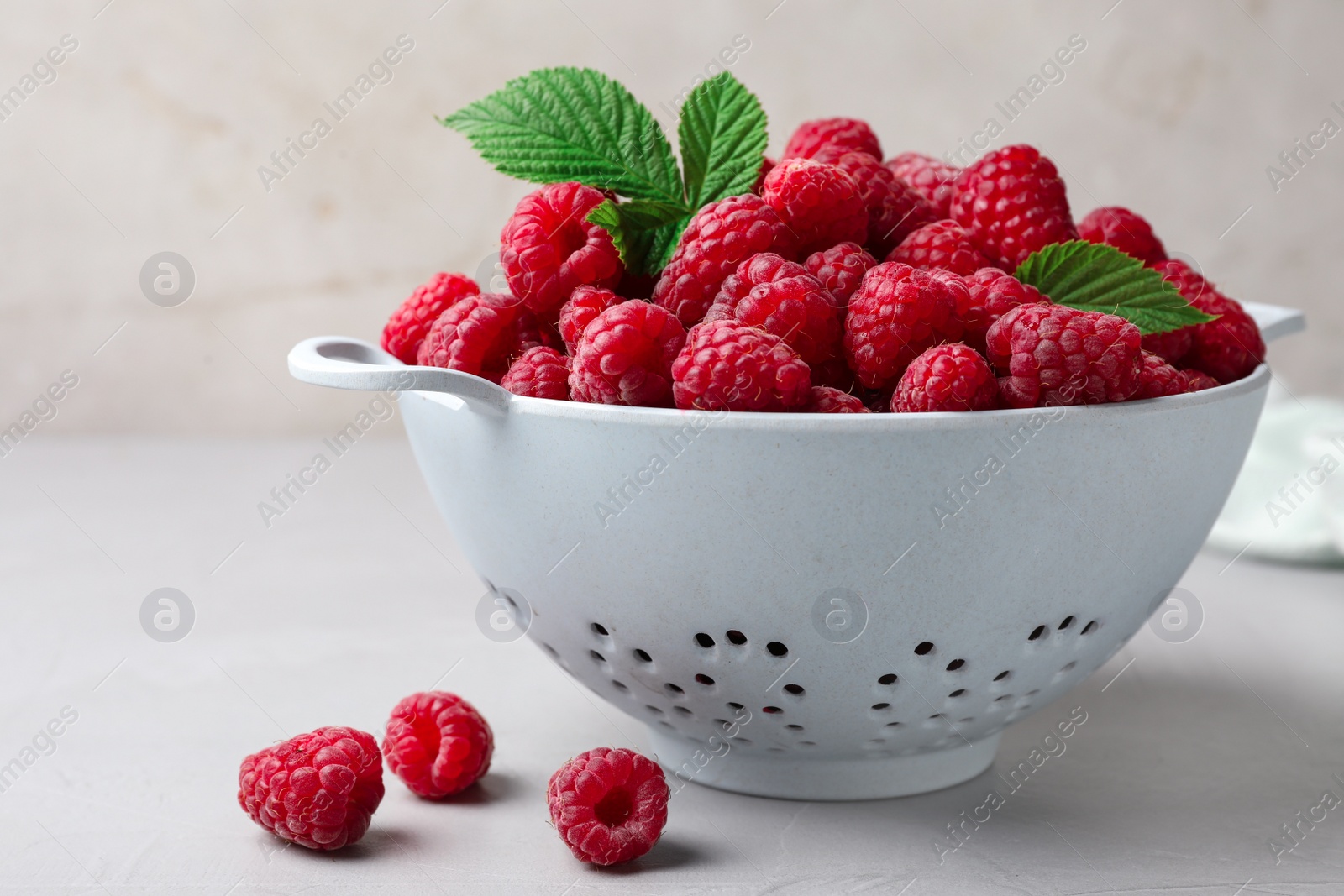 Photo of Colander with delicious ripe raspberries on table against light background, closeup