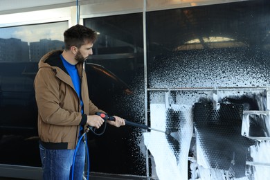 Man cleaning auto mats with high pressure water jet at self-service car wash