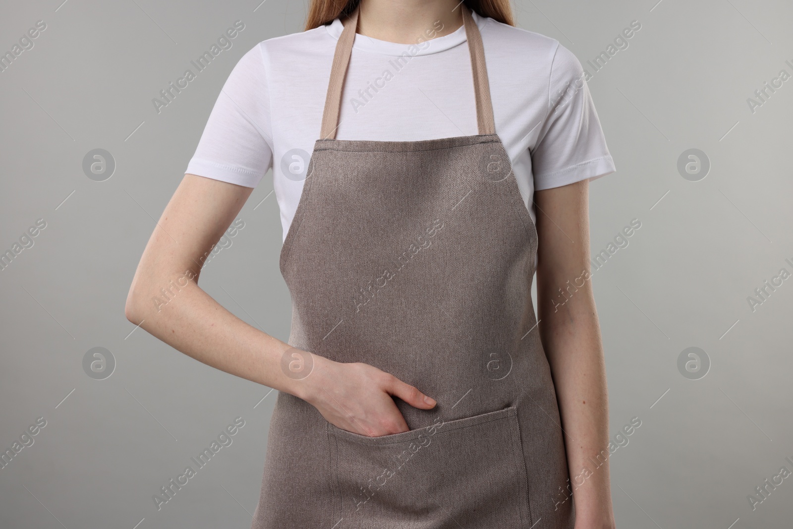 Photo of Woman wearing kitchen apron on grey background, closeup. Mockup for design