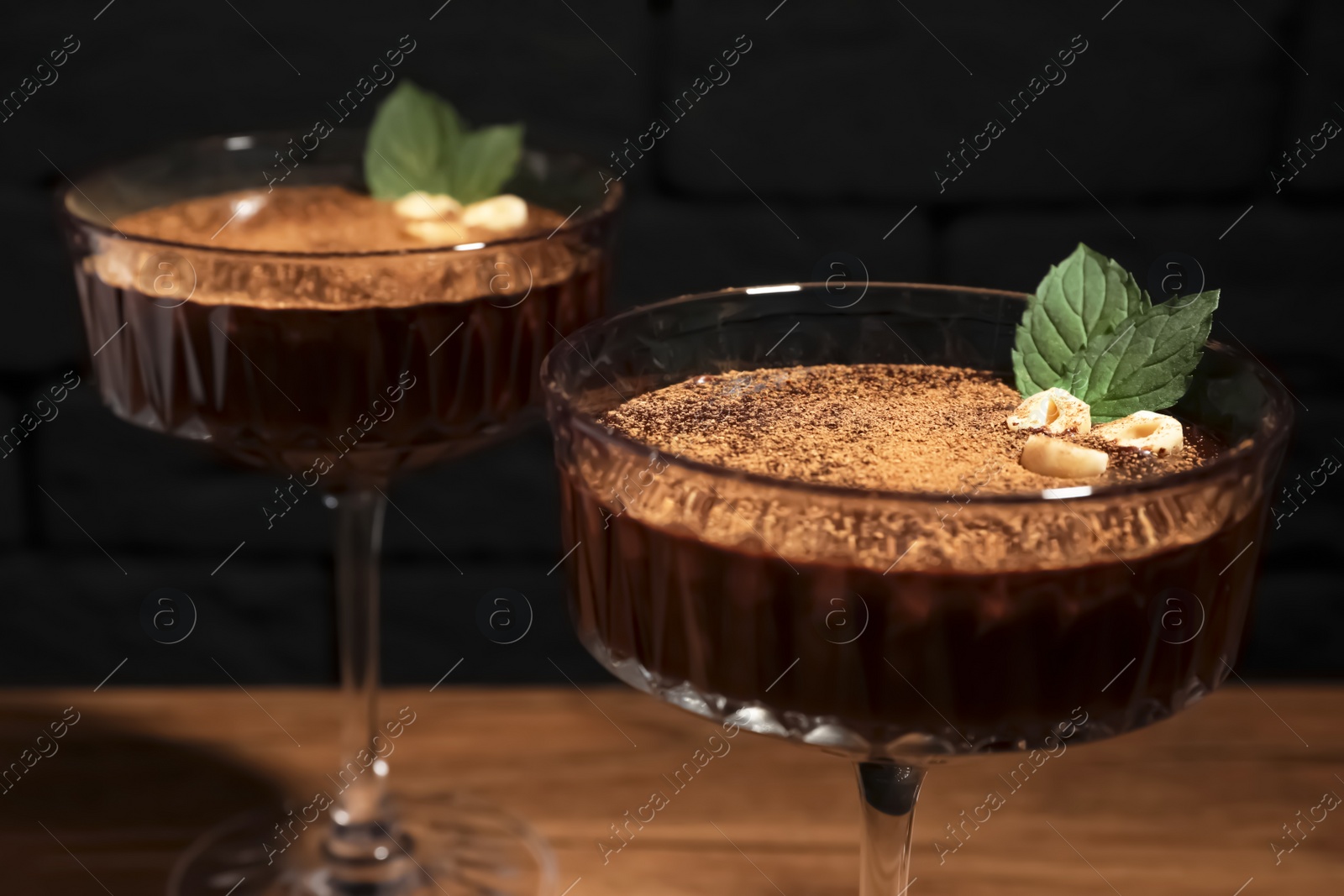 Photo of Dessert bowls of delicious hot chocolate with hazelnuts and fresh mint on wooden table, closeup