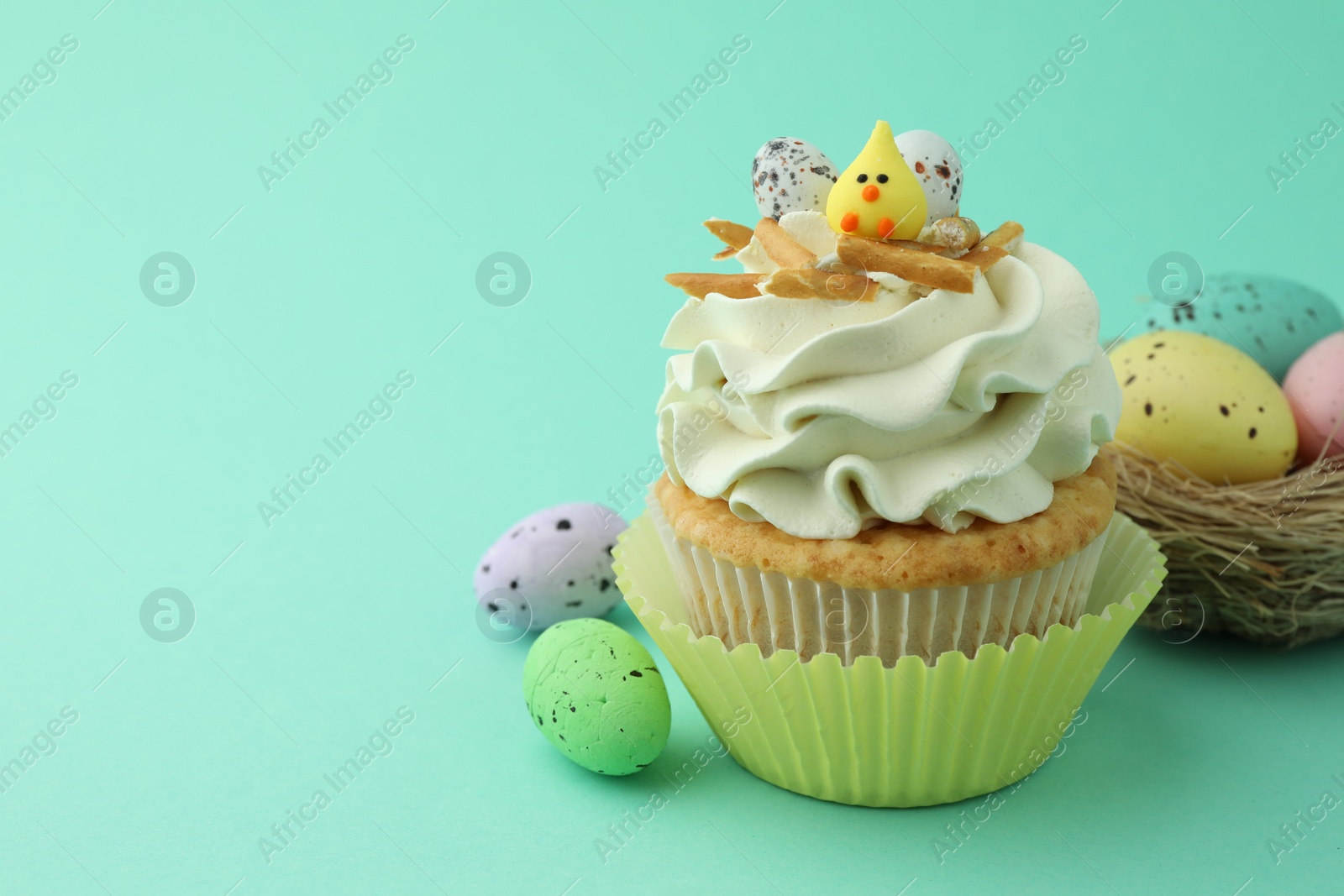 Photo of Tasty Easter cupcake with vanilla cream and festive decor on turquoise background, space for text