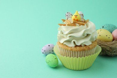 Photo of Tasty Easter cupcake with vanilla cream and festive decor on turquoise background, space for text