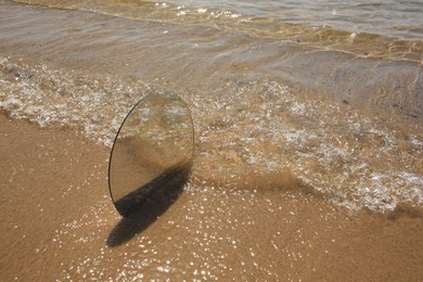 Photo of Round mirror reflecting sea on sandy beach, space for text