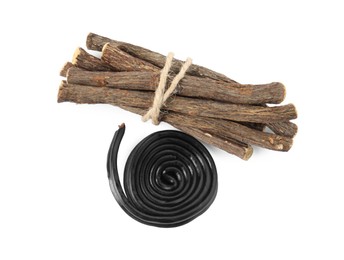 Photo of Tasty black candy and dried sticks of liquorice root on white background, top view