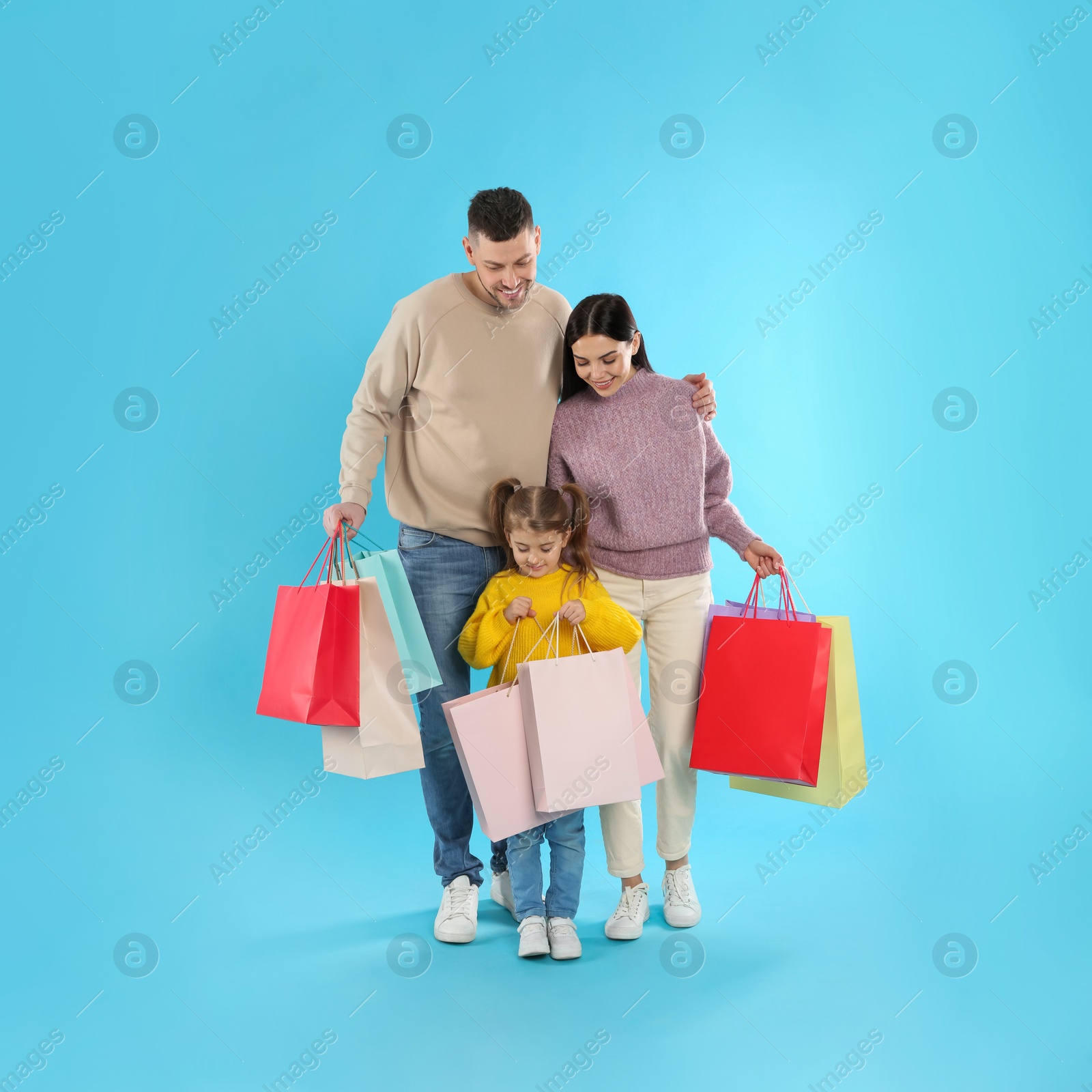 Photo of Happy family with paper bags on light blue background. Christmas shopping