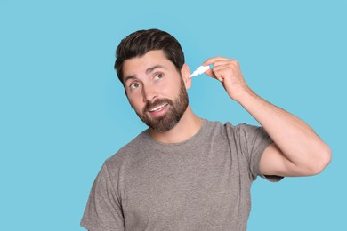 Man using ear drops on light blue background