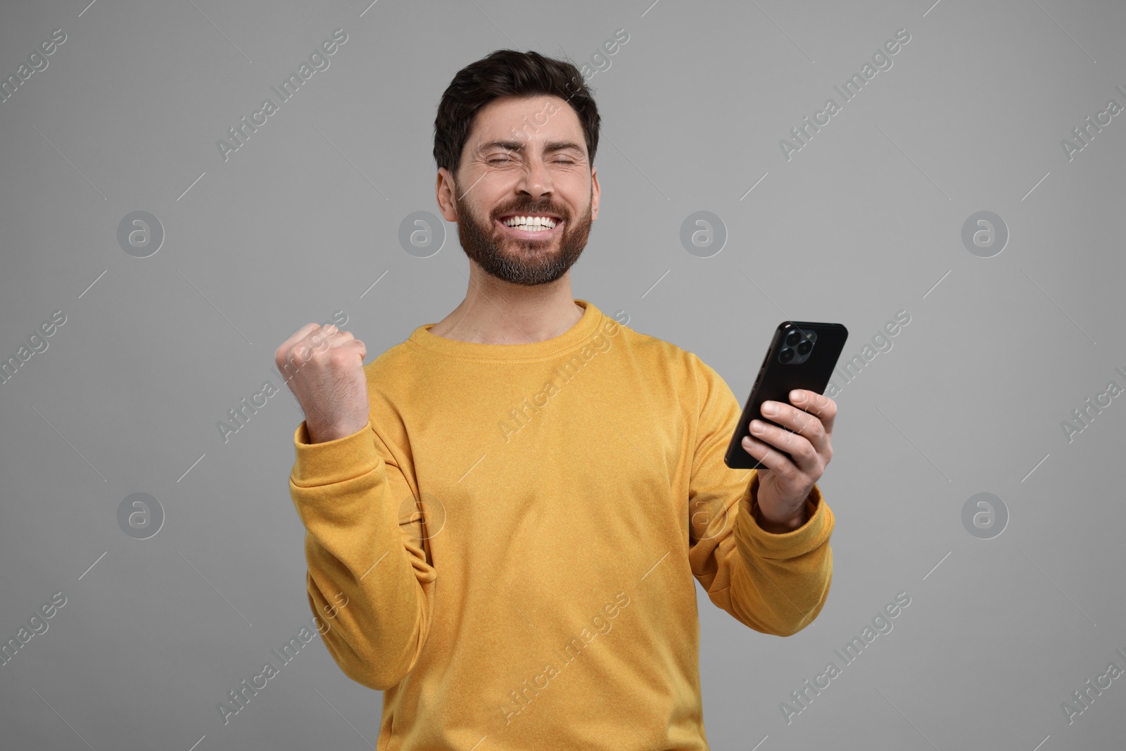 Photo of Smiling man with smartphone on grey background