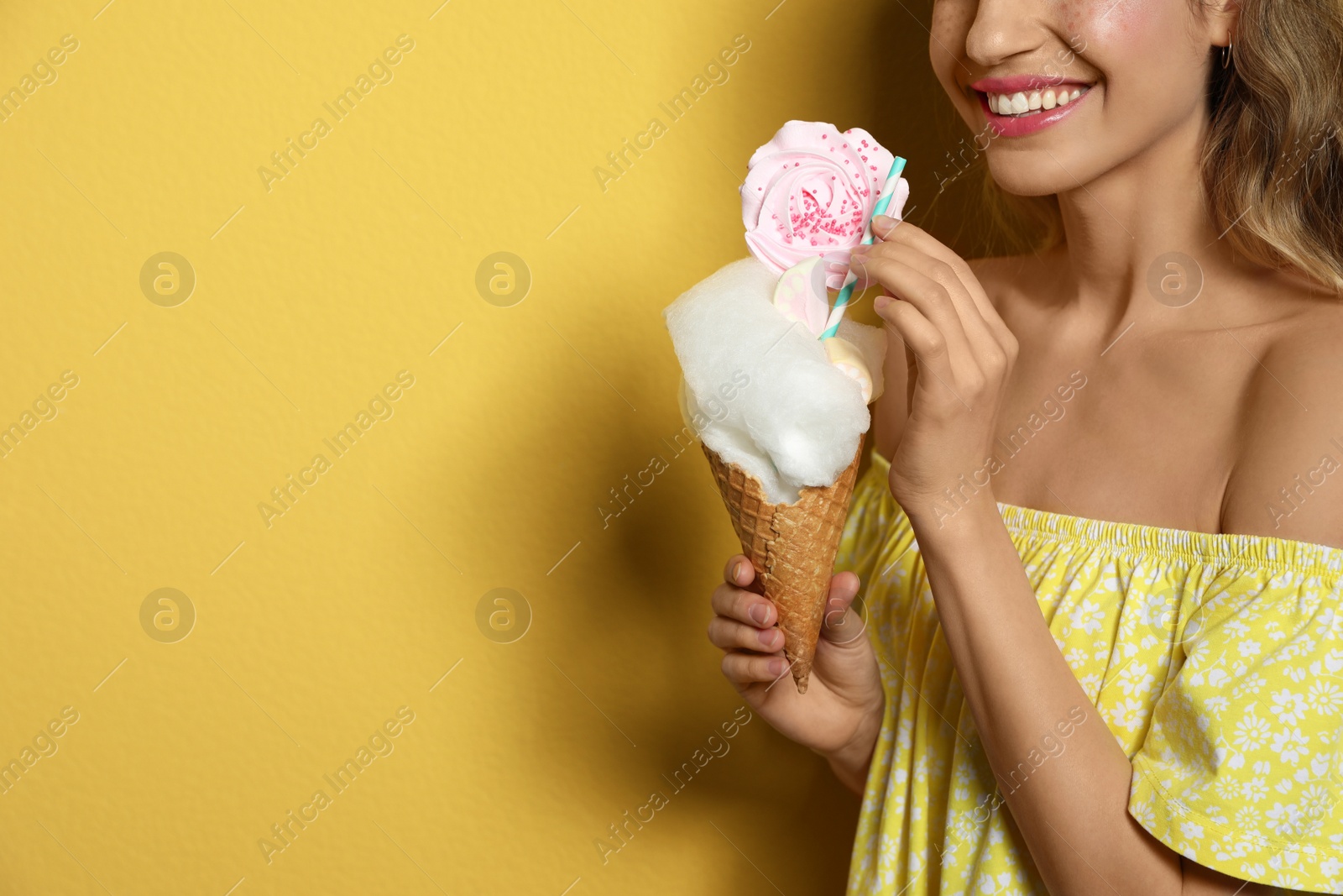 Photo of Young woman holding cotton candy dessert on yellow background, closeup. Space for text