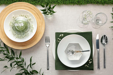 Elegant table setting with green plants on light cloth, flat lay