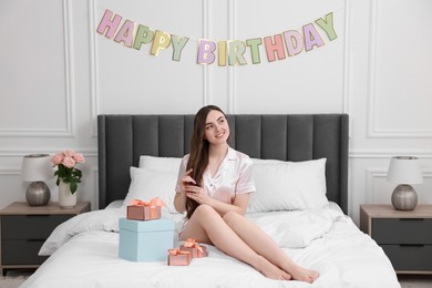 Photo of Beautiful young woman with headband and gift boxes on bed in room. Happy Birthday