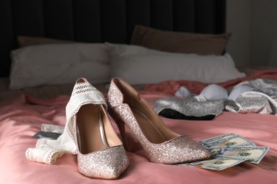 Photo of Prostitution concept. High heeled shoes, dollar banknotes and panties on bed