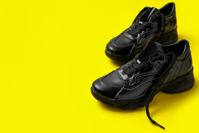 Stylish black sneakers on yellow background, space for text