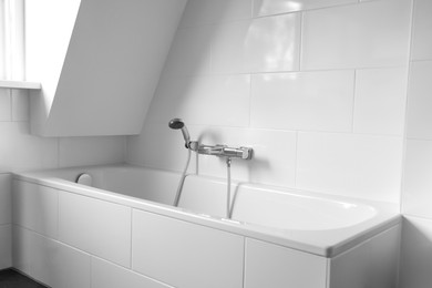 Photo of Clean tub with showerhead and tap in white bathroom. Interior design