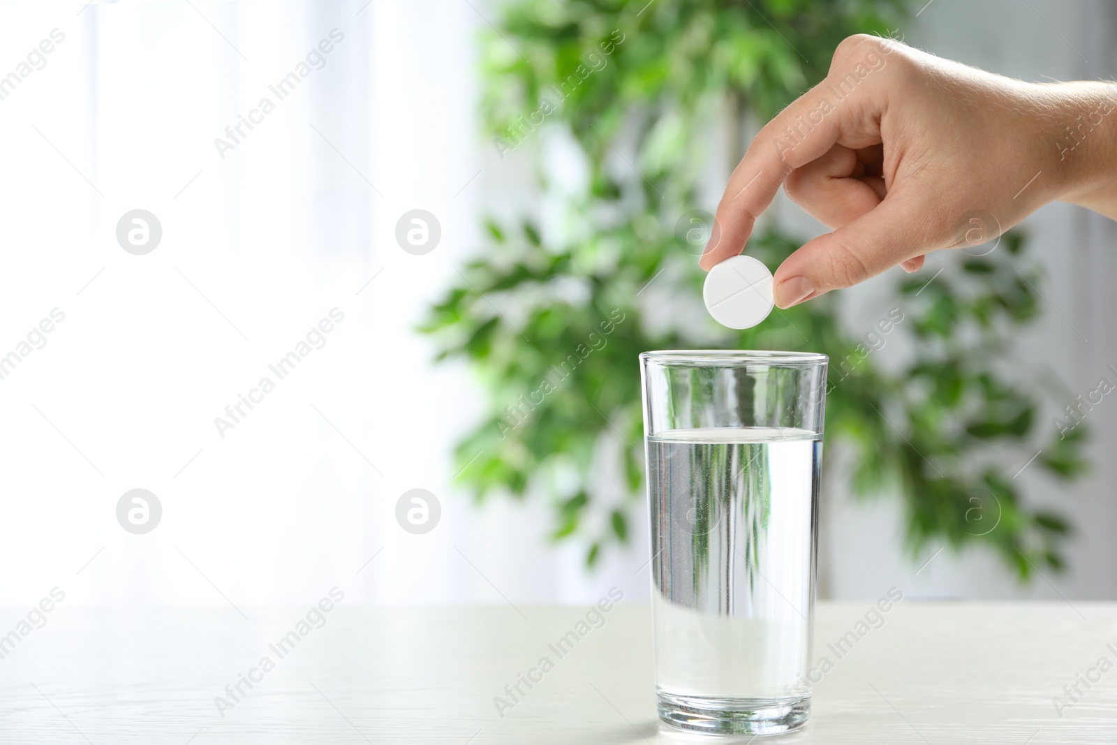 Photo of Woman putting tablet into glass of water indoors, space for text