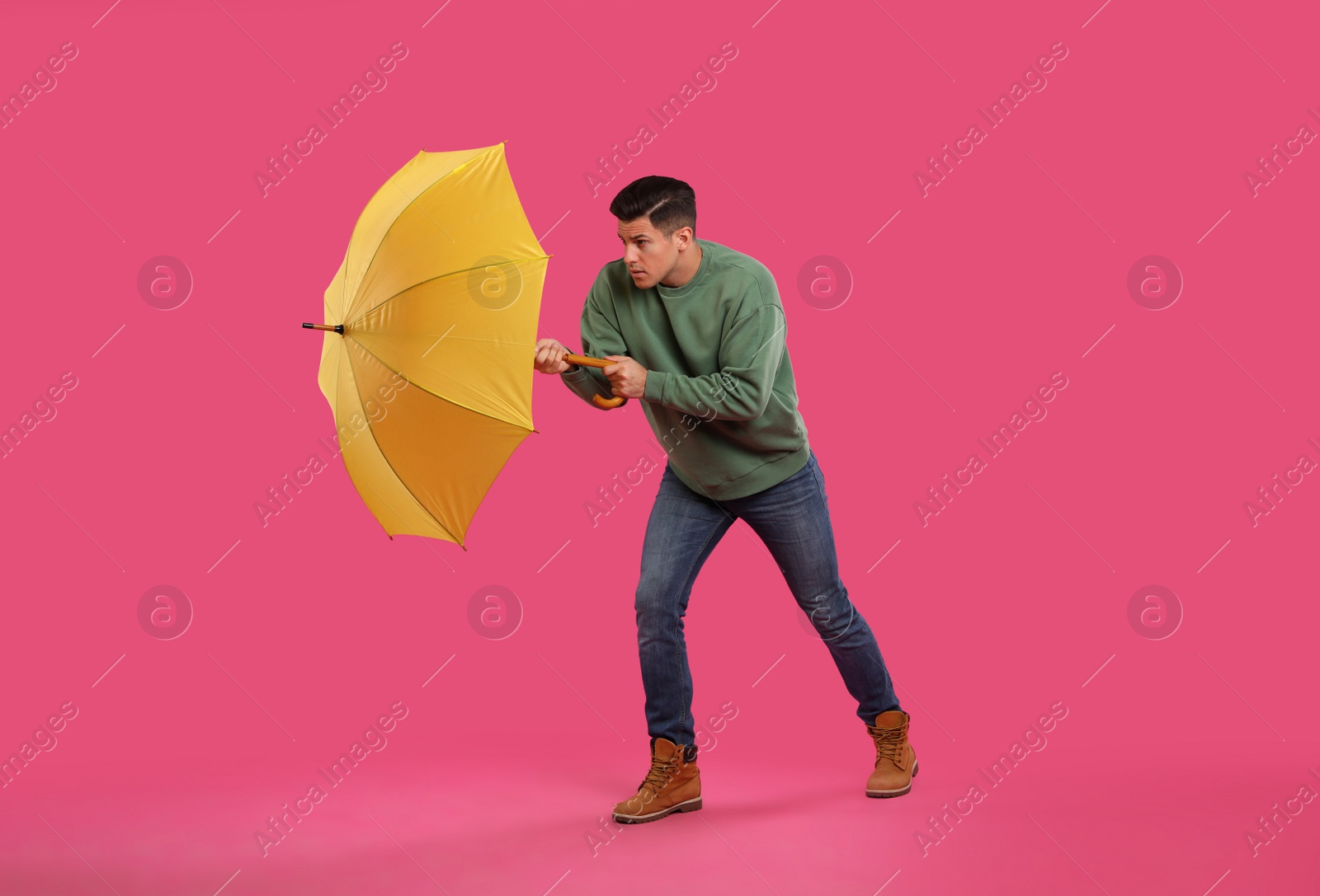 Photo of Emotional man with umbrella caught in gust of wind on pink background