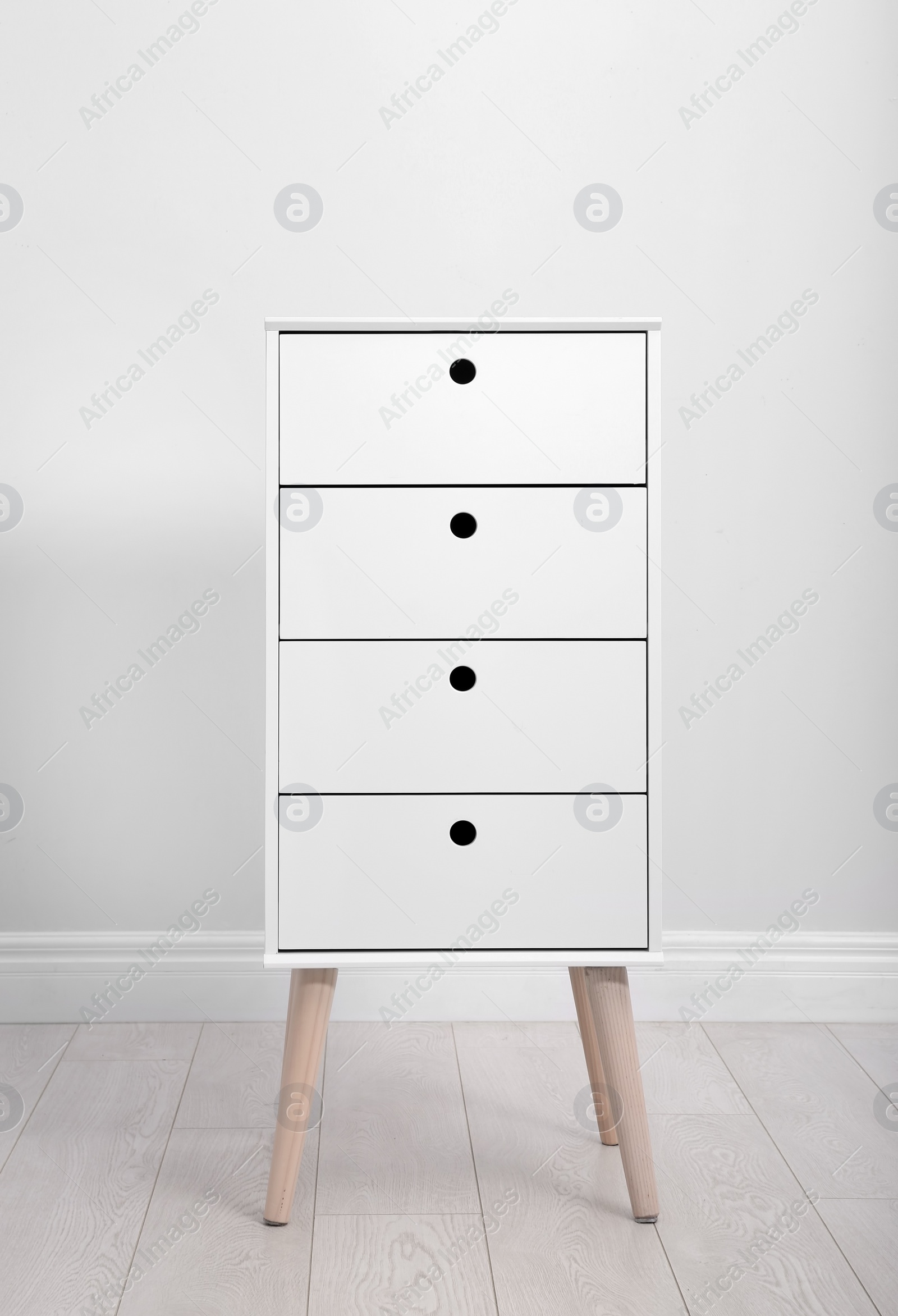 Photo of Stylish chest of drawers near white wall. Furniture for wardrobe room