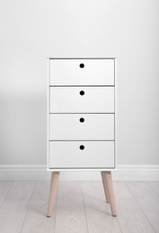 Photo of Stylish chest of drawers near white wall. Furniture for wardrobe room