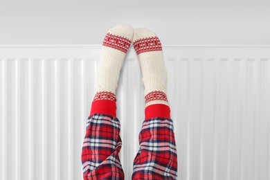 Little girl warming feet near heating radiator indoors, closeup