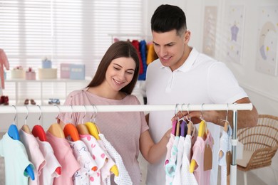 Photo of Happy pregnant woman with her husband choosing baby clothes in store. Shopping concept